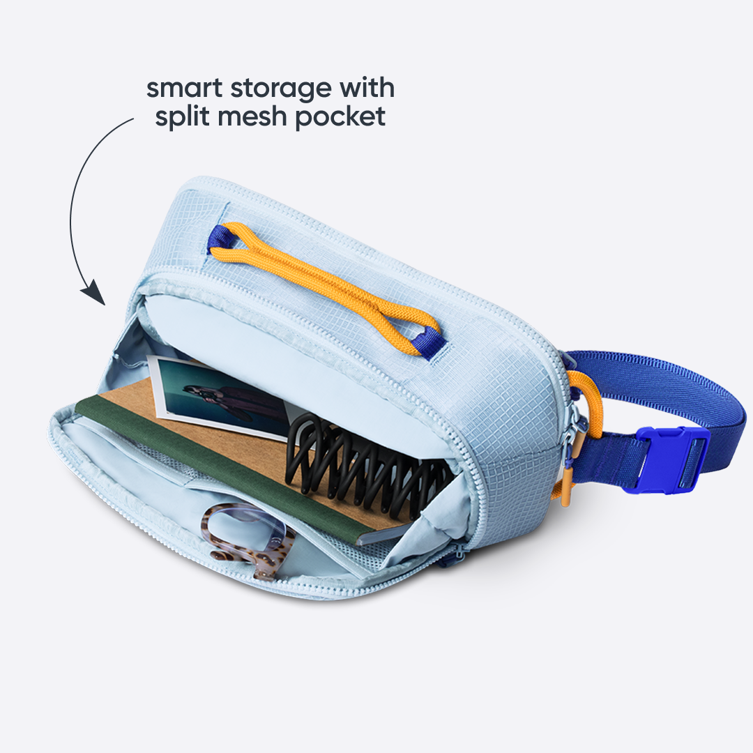 Owala All-Day Crossbody in Rest Azured, pale blue ripstop body with orange zipper pulls unzipped to show internal split mesh pocket with cards and essentials, with text reading "smart storage with split mesh pocket"